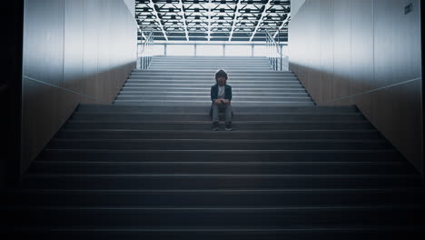 stressed schoolboy stay alone on stairway close up. boy hiding in school hall.