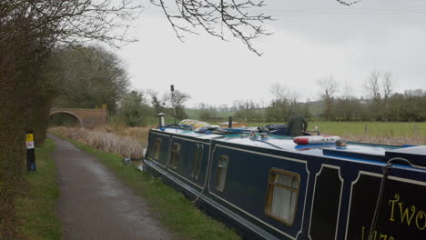 a canal narrow house boat passing along a river towards a bridge in the rain