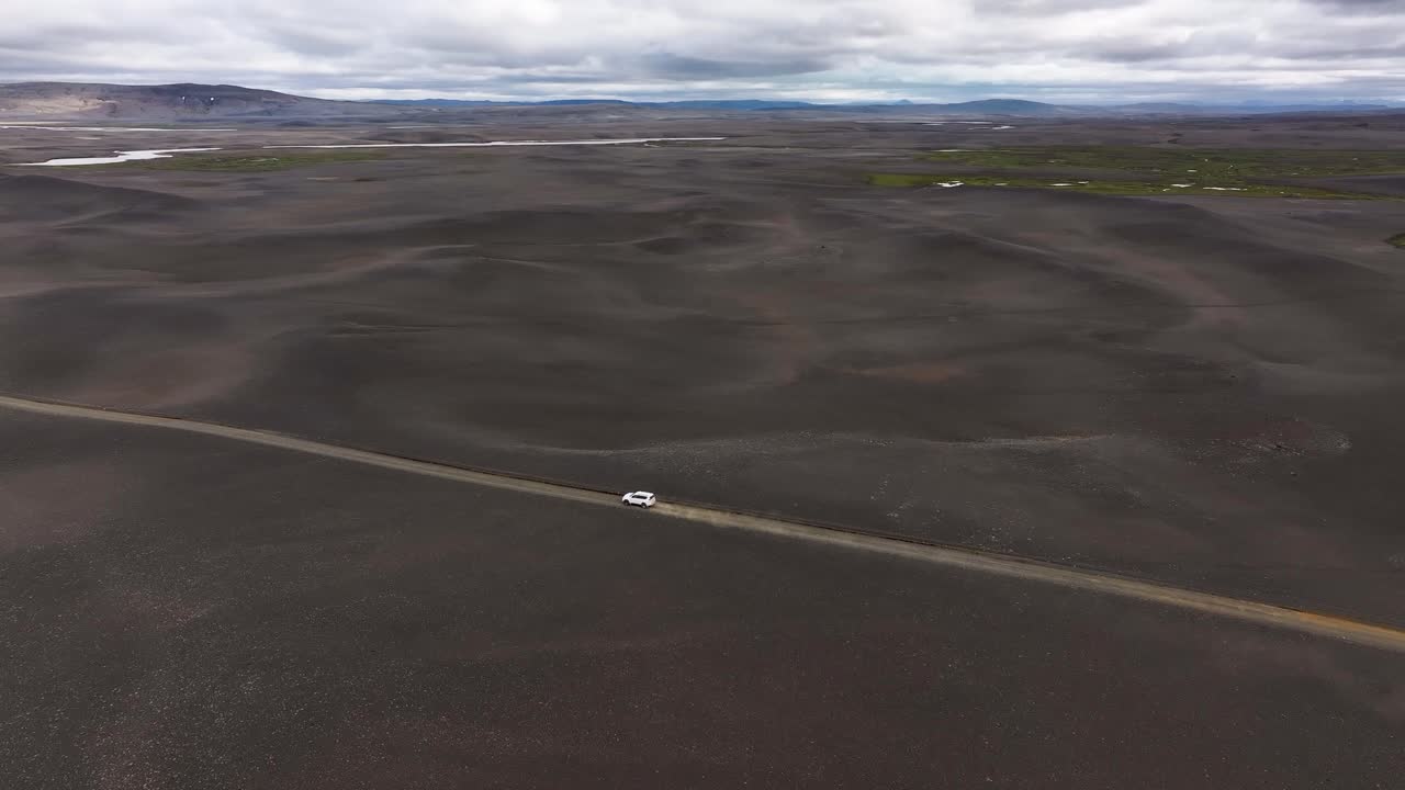 Distance mountains appear on the horizon as a white SUV overlanding the highlands of Iceland kicks up a dust cloud as it explores the off-road beauty of the land of fire and ice