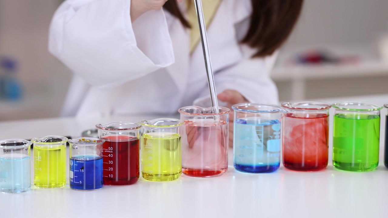 Primo piano di uno scienziato in camice bianco da laboratorio che mescola soluzioni chimiche vivaci usando pipette.