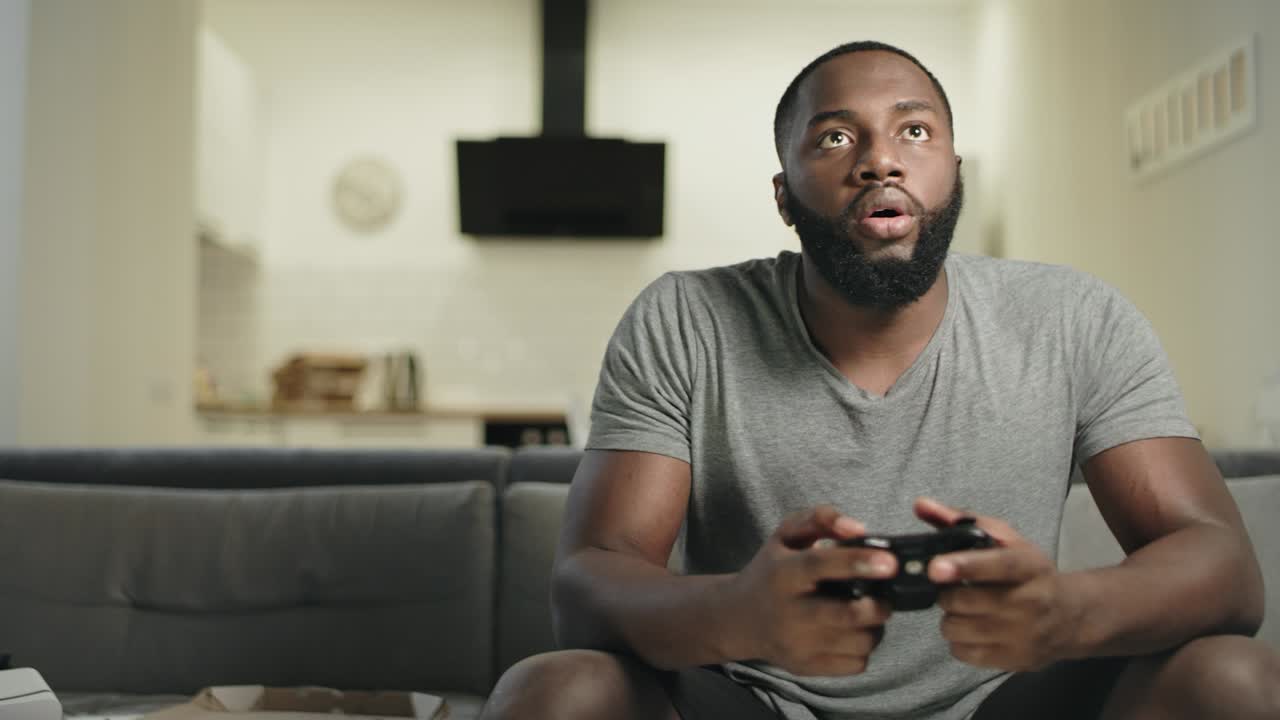 hombre negro sonriente jugando videojuegos en la cocina de su casa.