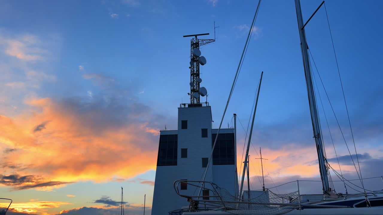 Tramonto su una torre e barche in un porto durante le ore serali. Una torre si erge alta accanto alle barche mentre il sole tramonta, riempiendo il cielo di colori.