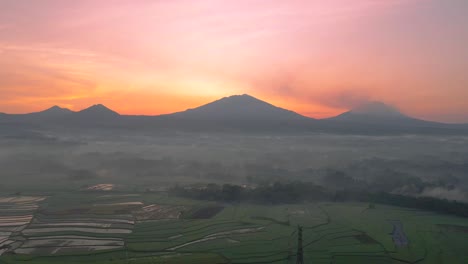 Luftaufnahme-Eines-Reisfeldes-Mit-Bergkette-Und-Sonnenaufgangshimmel-Bei-Leicht-Nebligem-Wetter