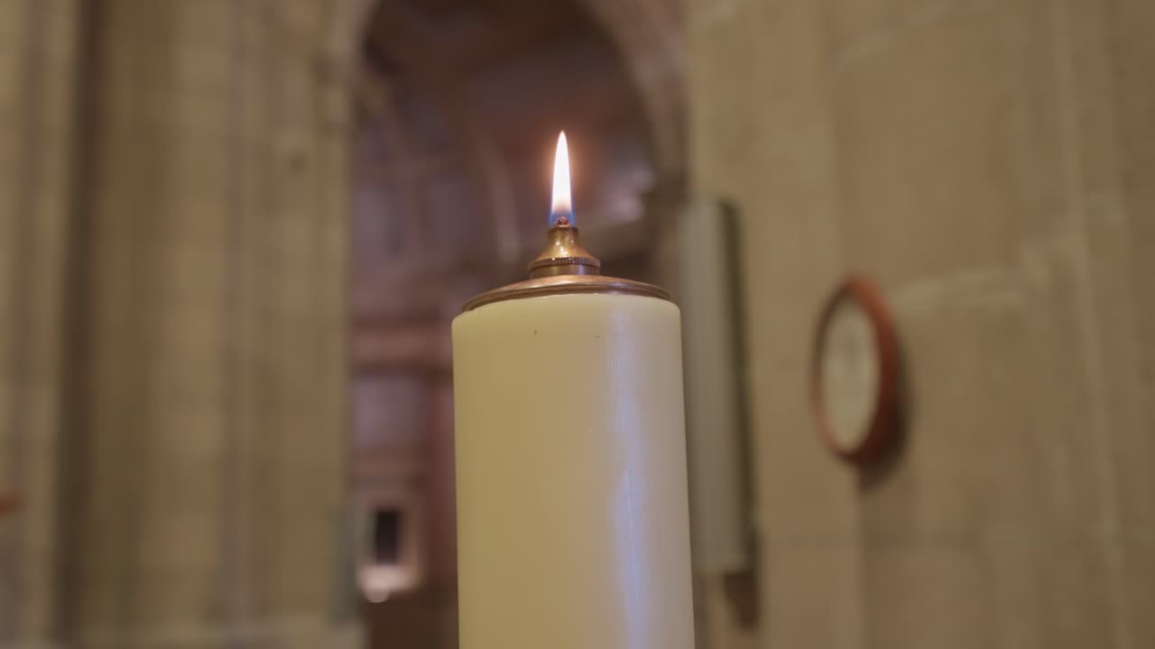 primer plano de la llama de una vela que brilla en el ambiente interior de una iglesia