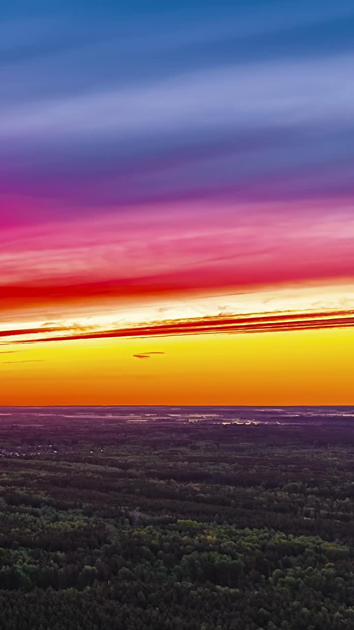 Wide sunset horizon with vibrant layered orange sky above forest in drone hyperlapse