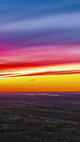 wide sunset horizon with vibrant layered orange sky above forest in drone hyperlapse
