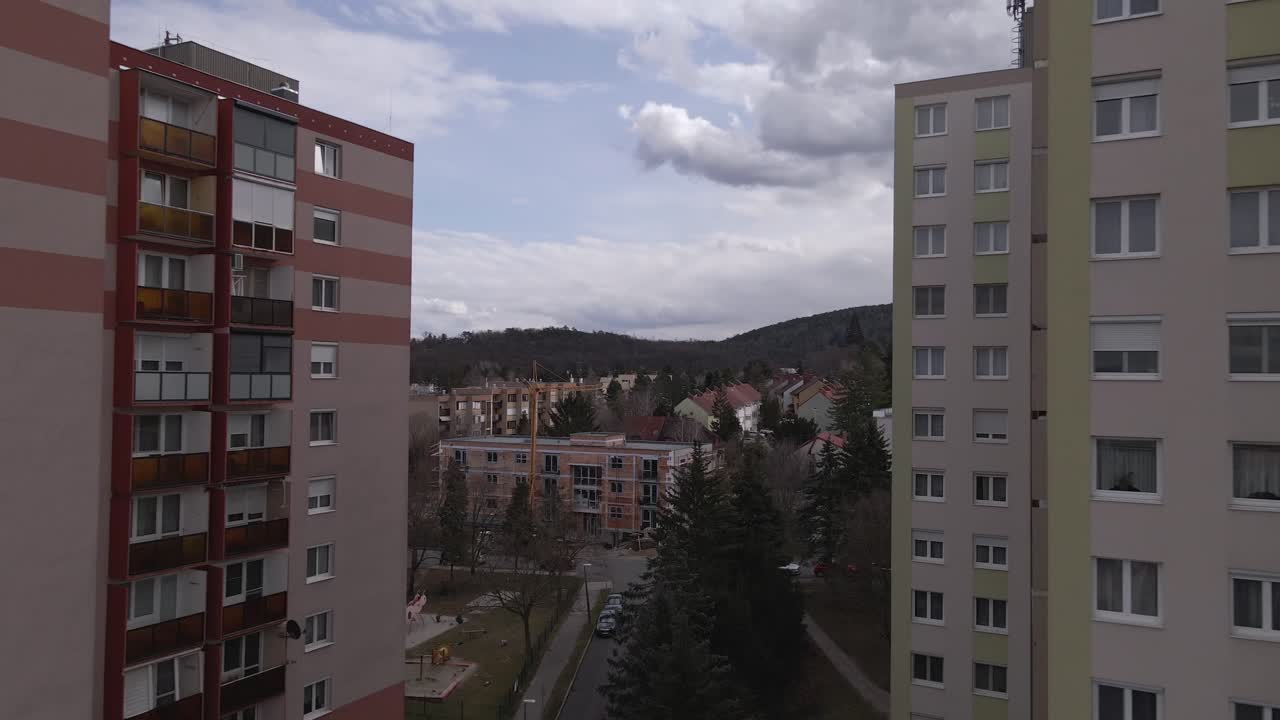 Flying between two apartment buildings with a drone, surrounded by an expansive rural landscape.