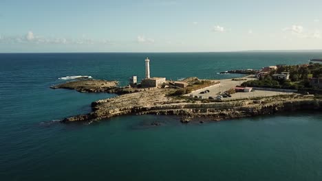 Drone-flyby-of-a-white-lighthouse-at-the-Mediterranean-coastline-of-Sicily,-Italy