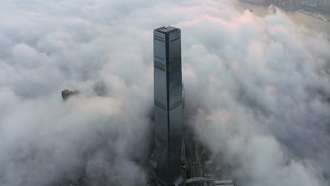 wide panning shot of the skyscraper icc above low morning clouds in hong kong