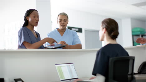 diverse female doctors discussing work, using tablet at reception desk at hospital, slow motion