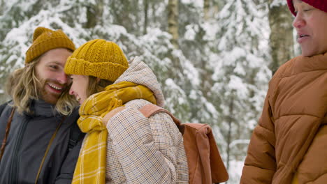 Close-Up-View-Of-Three-Friends-Sitting-On-A-Tree-Trunk-In-A-Snowy-Forest