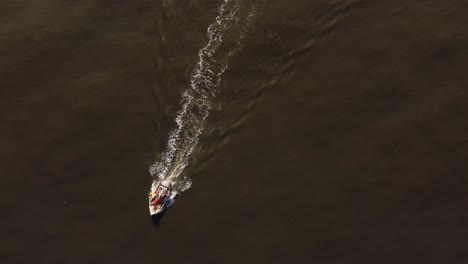 Isolated-fishing-motorboat-leaves-long-white-wake-trail-over-brown-and-calm-sea-water