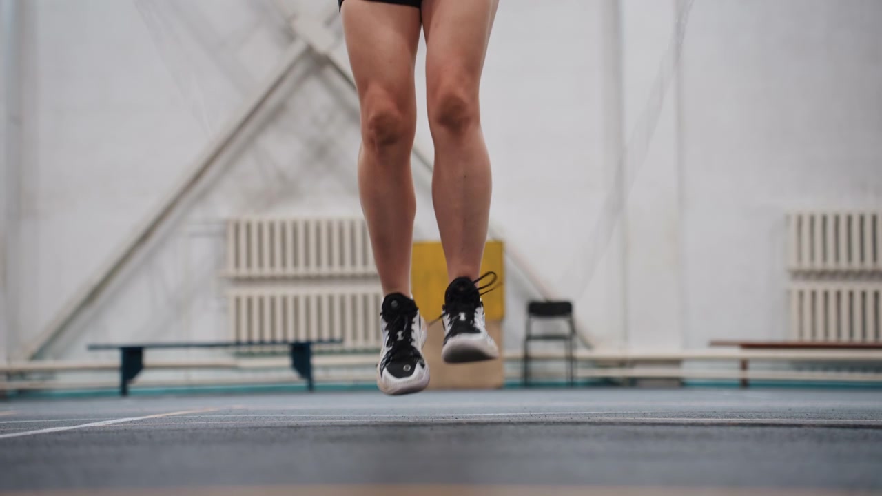 Indoor court jump rope warmup legs, closeup of athletic legs performing rapid rope hops and footwork drills on marked badminton court lines, lowangle perspective, sneakers hitting rubber surface