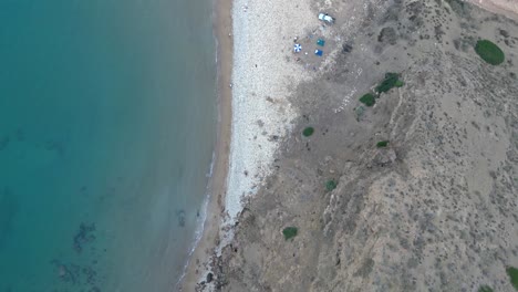 An-aerial-perspective-of-a-deserted-shoreline-featuring-a-magnificent-cliff-backdrop-and-crystal-clear-turquoise-waters