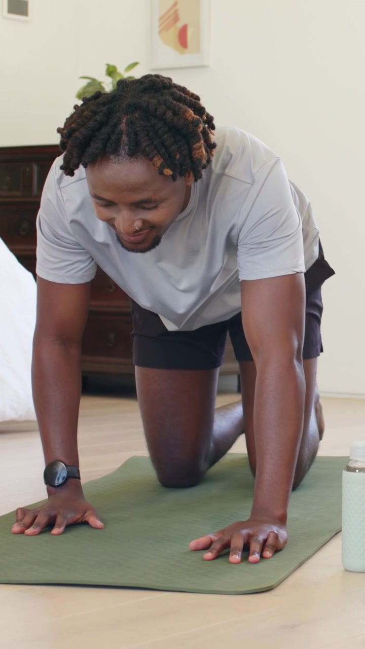 Fit man kneeling on green mat, lowering gaze, placing palms, shifting into tabletop for fitness