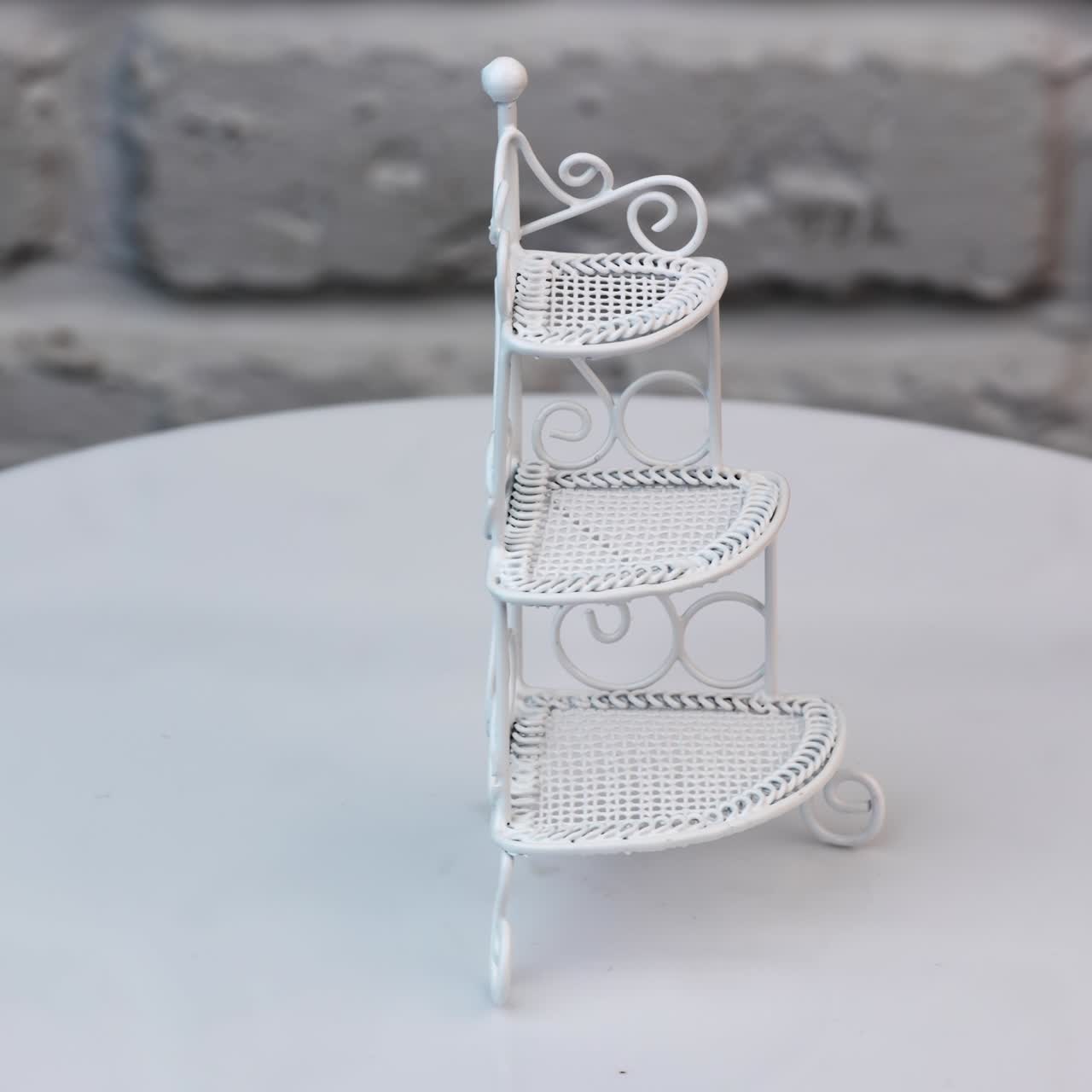 Beautiful ornamented shelf-stand rotating at the table. Toy furniture item for doll's house at the backdrop of white brick wall