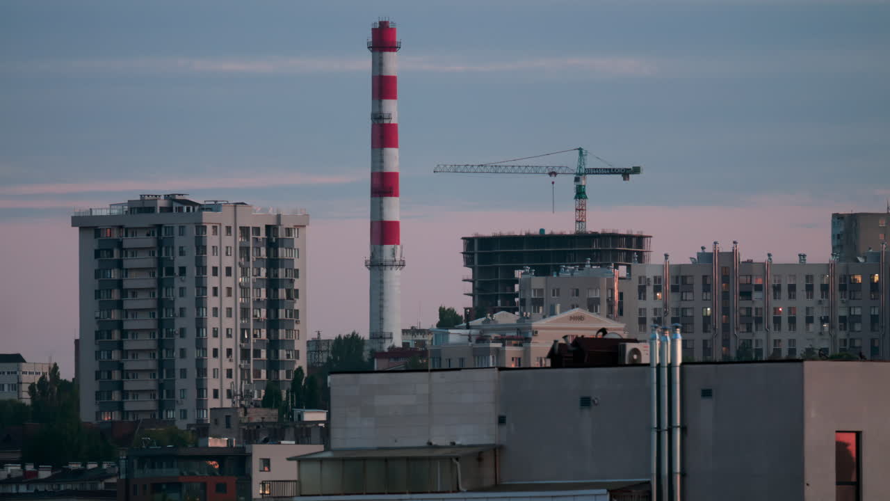 City skyline with construction crane and red white chimney in soft evening light