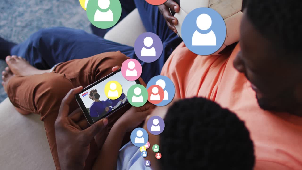 Animation of social media icons over african american father and son watching football on smartphone