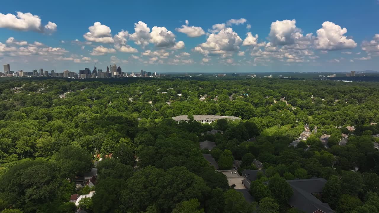 Panoramic drone shot of green city in Atlanta, Georgia. Dense trees in Suburbia with homeward houses. Downtown skyline with skyscrapers in background. Panning wide shot. Georgia, USA in summertime