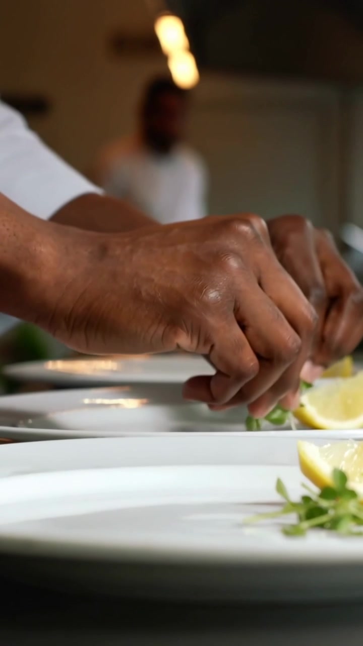 Video verticale: Chef che impiattano in giacca bianca, posizionando erbe aromatiche e limone sui piatti in cucina per il servizio