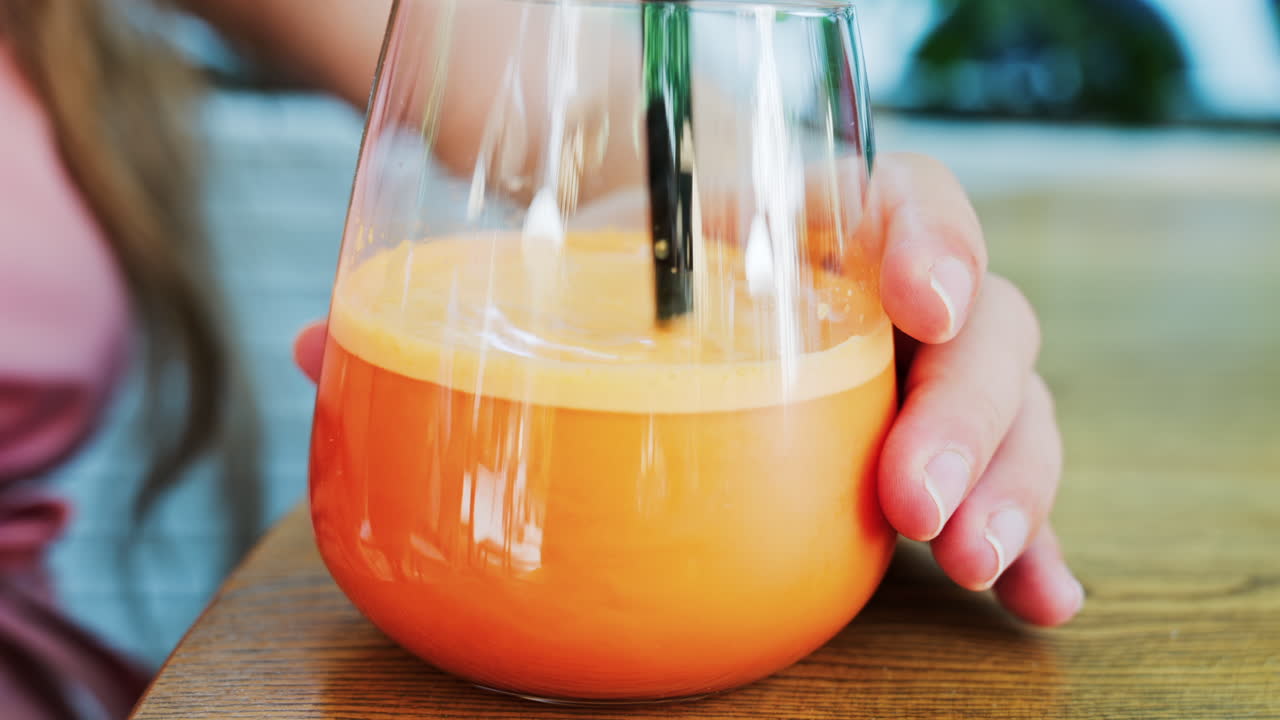 Close up of a woman mixing in a glass of orange juice with a black straw