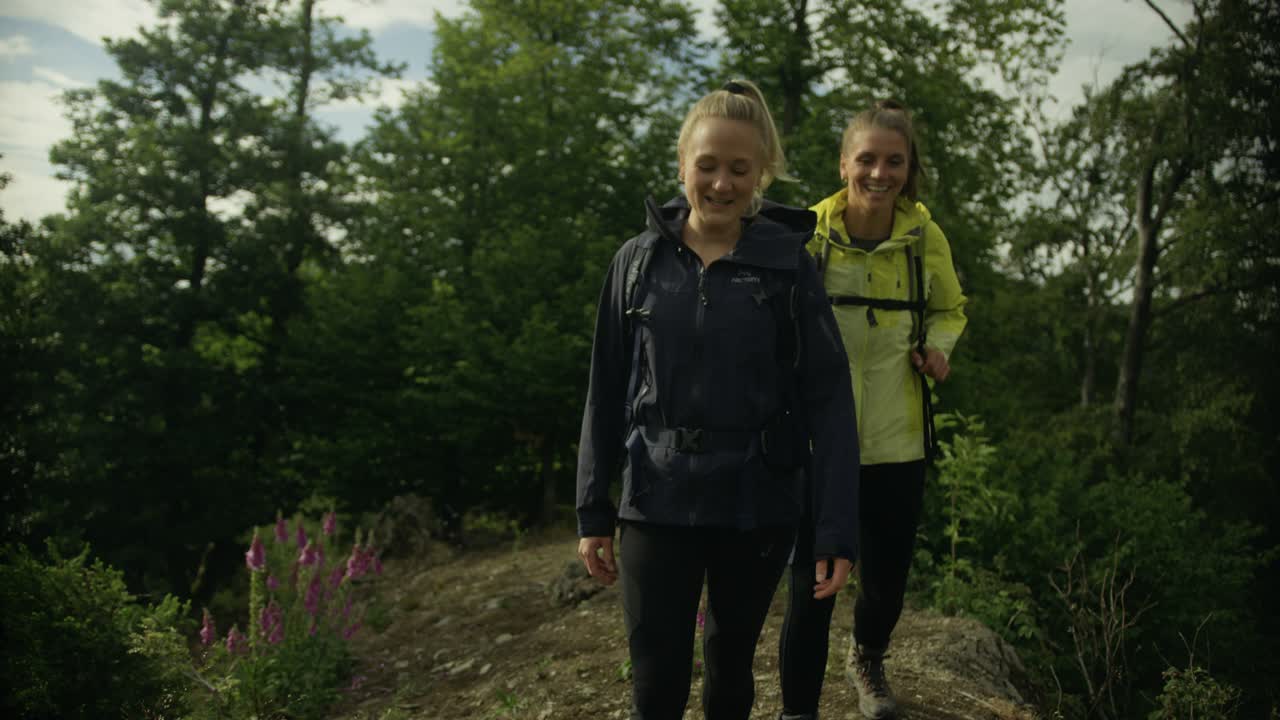 Two Happy Women Hiking through the Woods on a Hill. Walking through Nature. Looking at Landscapes. Connecting with Nature.