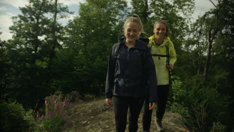 two happy women hiking through the woods on a hill. walking through nature. looking at landscapes. connecting with nature.
