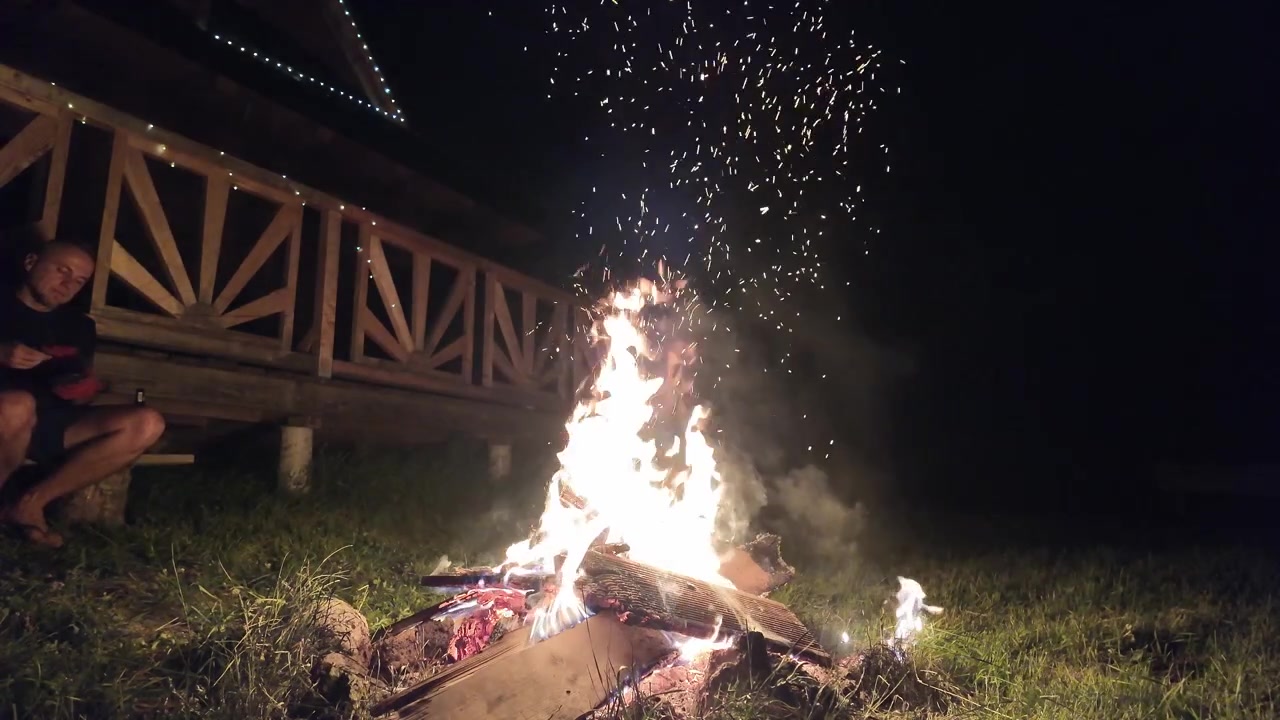 Grande fogueira acesa em um acampamento sob o céu noturno escuro. Brilho quente, brasas voando e ambiente natural ao ar livre ideal para visuais de viagem, acampamento e aventura.