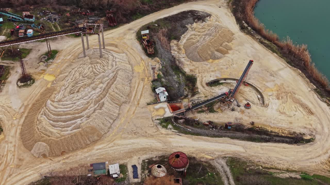 Sand quarry site with equipment and piles in a natural setting