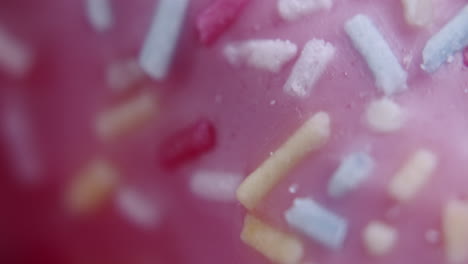 extreme macro shot of colored sprinkles on top of a pink donut. donut spins clockwise. shot with shallow depth of field.