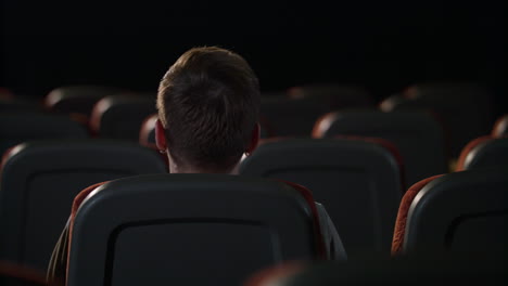 stylish guy sitting in empty movie theater alone. back view of man in cinema