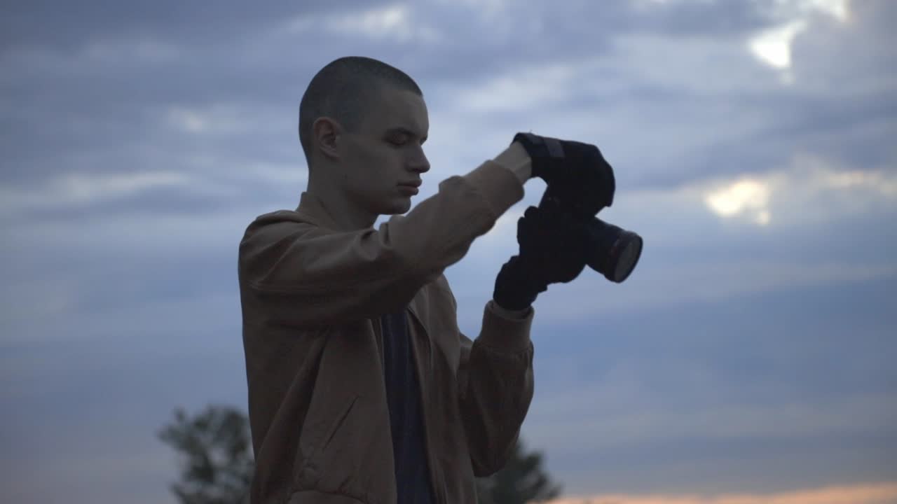 Jeune homme en manteau marron prenant des photos avec son appareil photo à la plage – Plan moyen (ralenti)