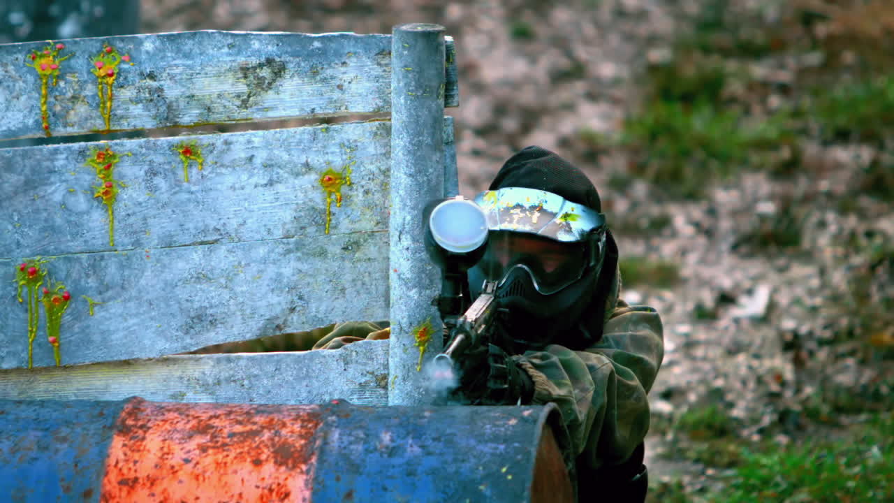 hombre disparando su arma de paintball escondiéndose detrás de la valla