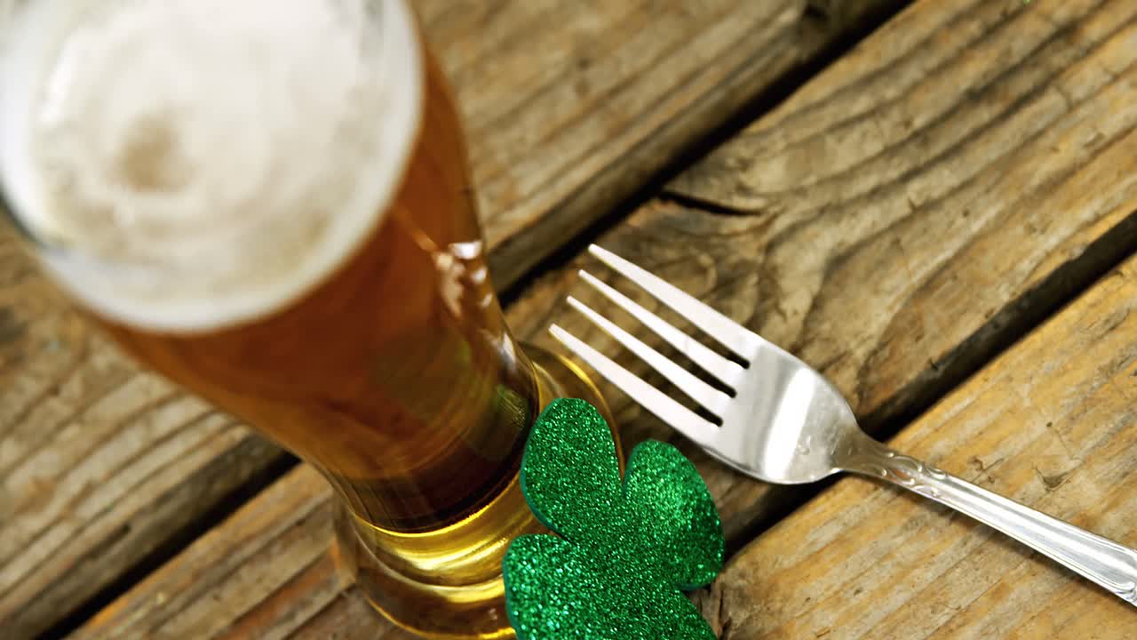 Close up view of pint of beer, fork and shamrock on wooden table for st patricks