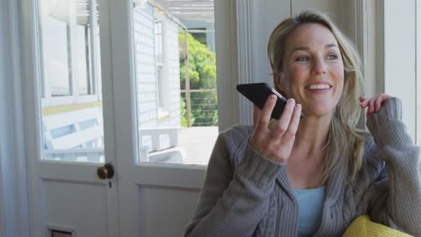 happy caucasian mature woman siting in living room and using smartphone