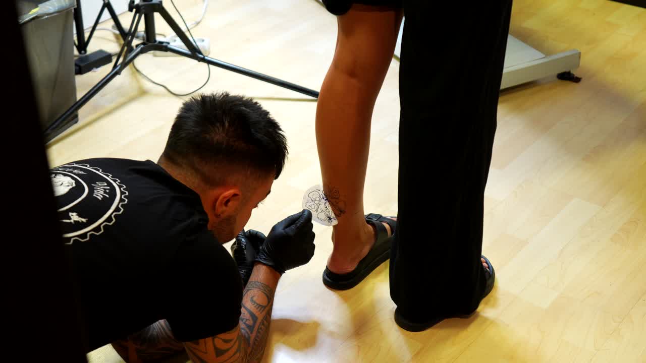 Tattoo artist applying stencil of design on client's lower leg before tattooing