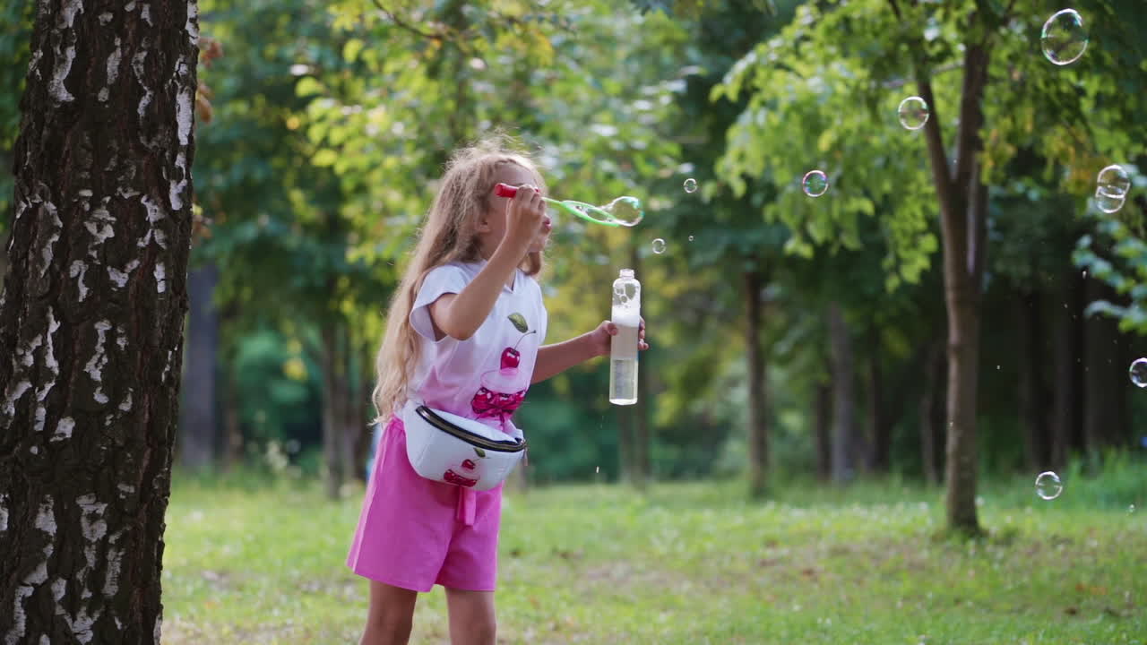 Little girl with bubble blower outdoors. Beautiful child blowing soap bubbles in the park. Happy girl with long hair blows shiny bubbles in the forest.