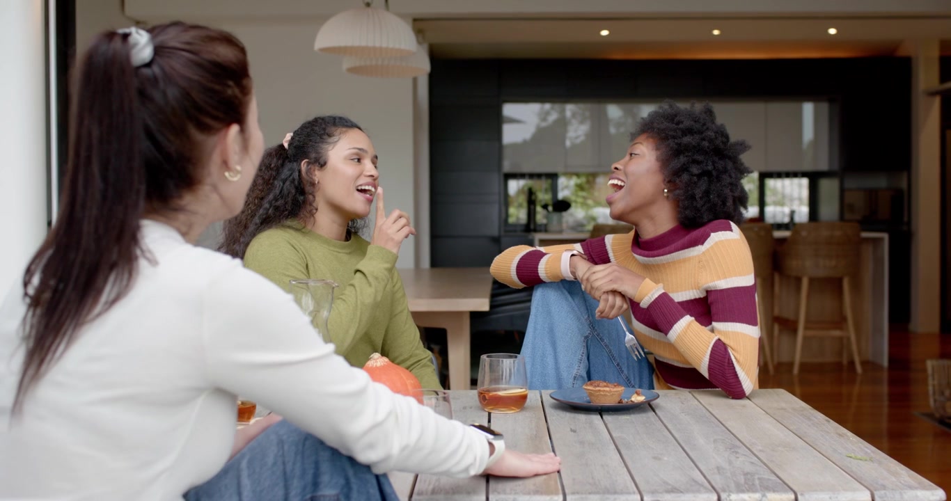 Female friends watching right woman in striped top starting story, gesturing fork to amuse at patio