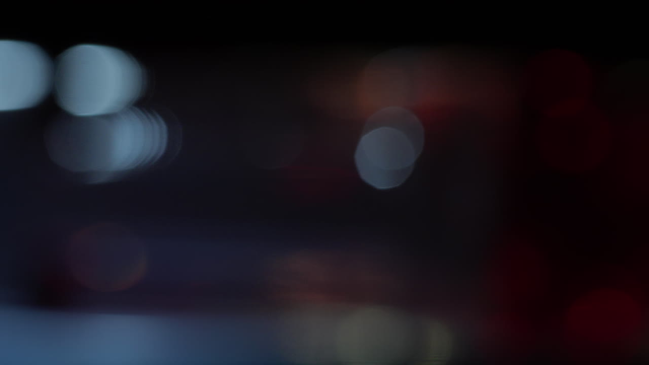 Slow motion analogue footage of abstract red and silver bokeh drifting through darkness. Handmade light refractions evoke a tactile, immersive feel ideal for overlays, design, or projection visuals.