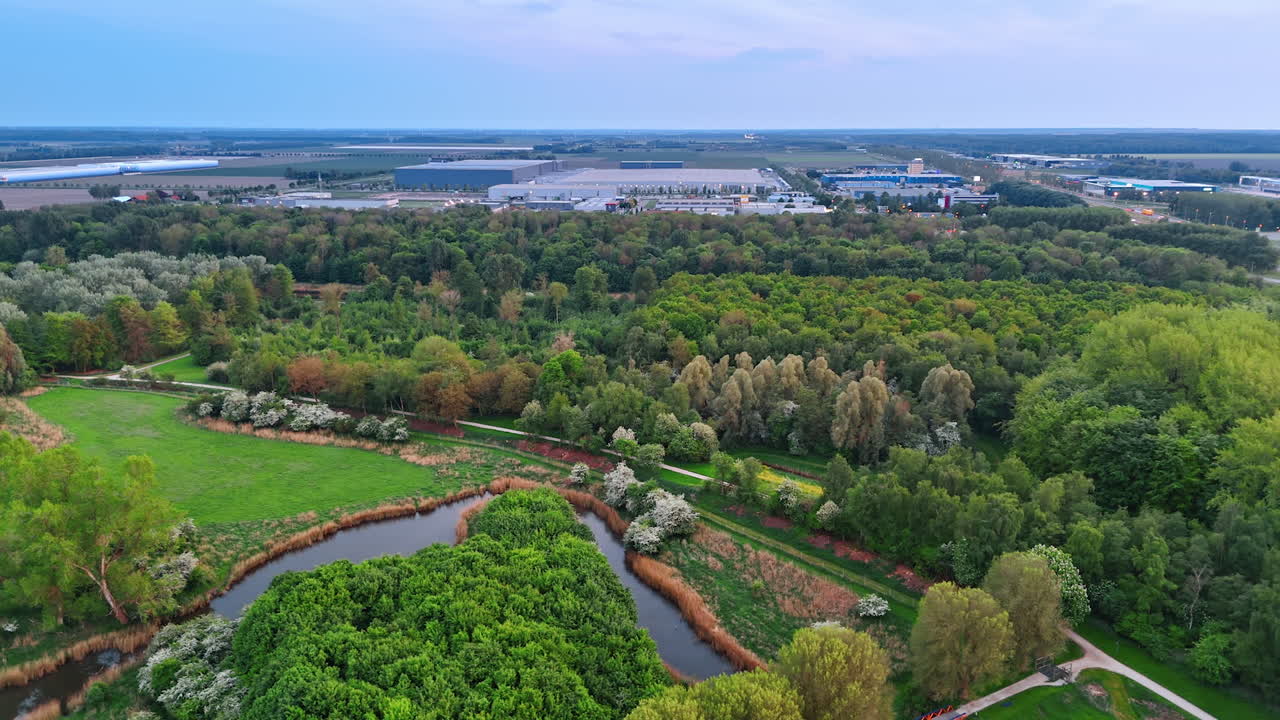 Lush green park with a narrow river. Large storehouses at backdrop. Picturesque countryside of the Netherlands. Top view.