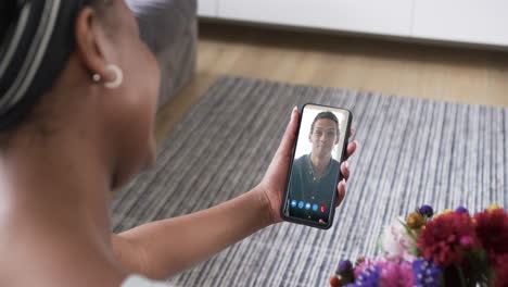 mujer afroamericana sosteniendo un teléfono inteligente con un hombre biracial en la pantalla