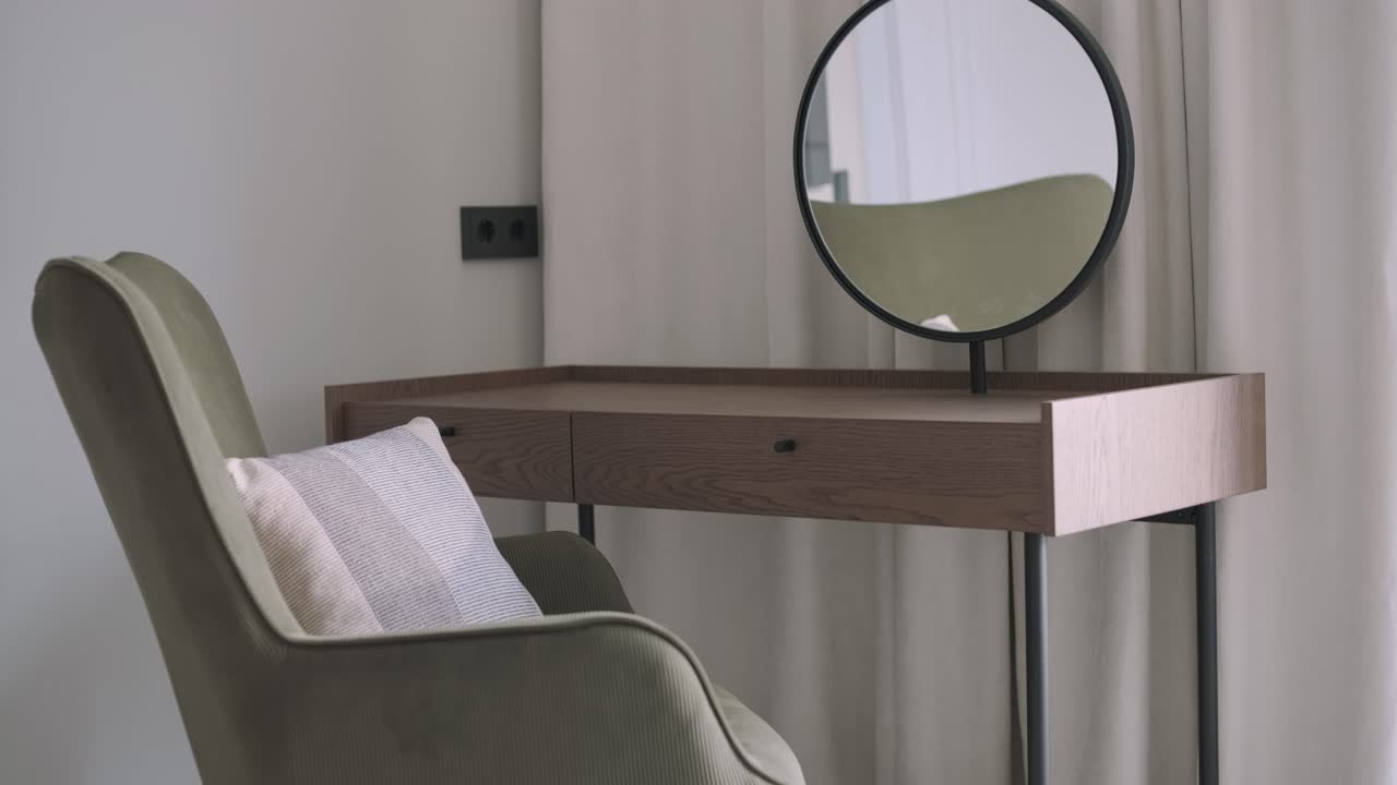 un vestidor minimalista con una elegante mesa de consola de madera con un espejo redondo, complementado por una peluche silla verde oliva y una almohada suave, creando un rincón tranquilo en un dormitorio moderno.