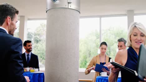 Business-executive-taking-coffee-from-coffee-maker-while-colleagues-interacting-with-each-other