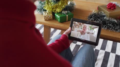 Caucasian-man-waving-and-using-tablet-for-christmas-video-call-with-smiling-woman-on-screen