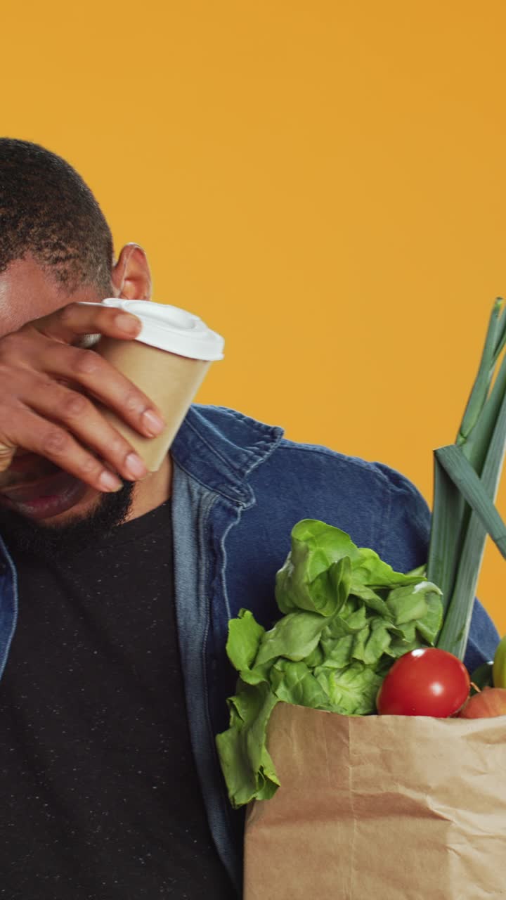 Jovem negro cansado bebe café e segura compras