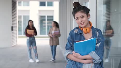 portrait of an asian college student holding folders and looking at the camera while standing at the hallway. education concept.
