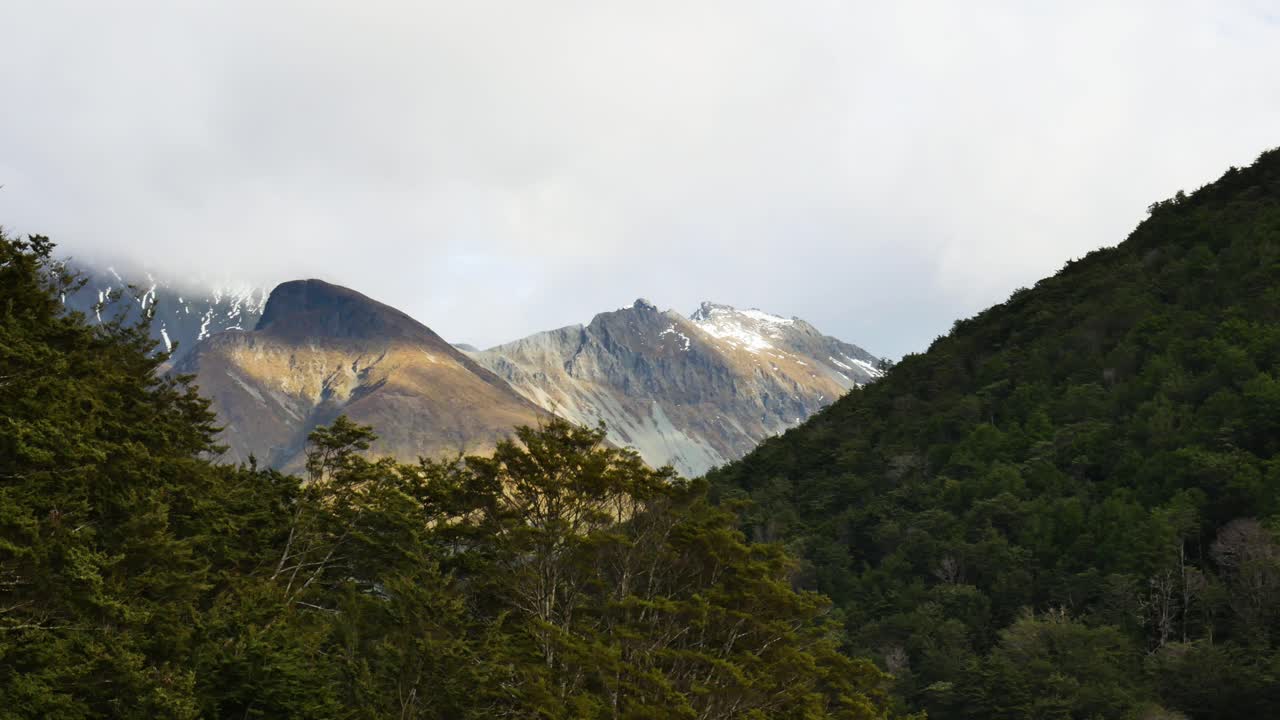 pan shot montañas boscosas con picos nevados en segundo plano.