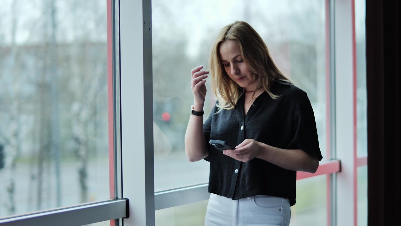 Donna controlla lo smartphone alla finestra, riflettendo i rischi per la privacy dei dati personali