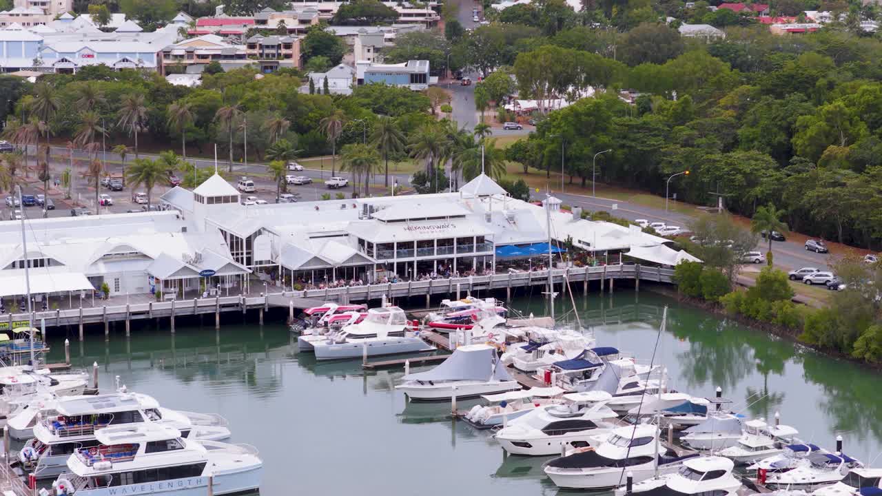 Aerial footage captures boats docked at Port Douglas marina, surrounded by lush greenery and calm waters under overcast skies