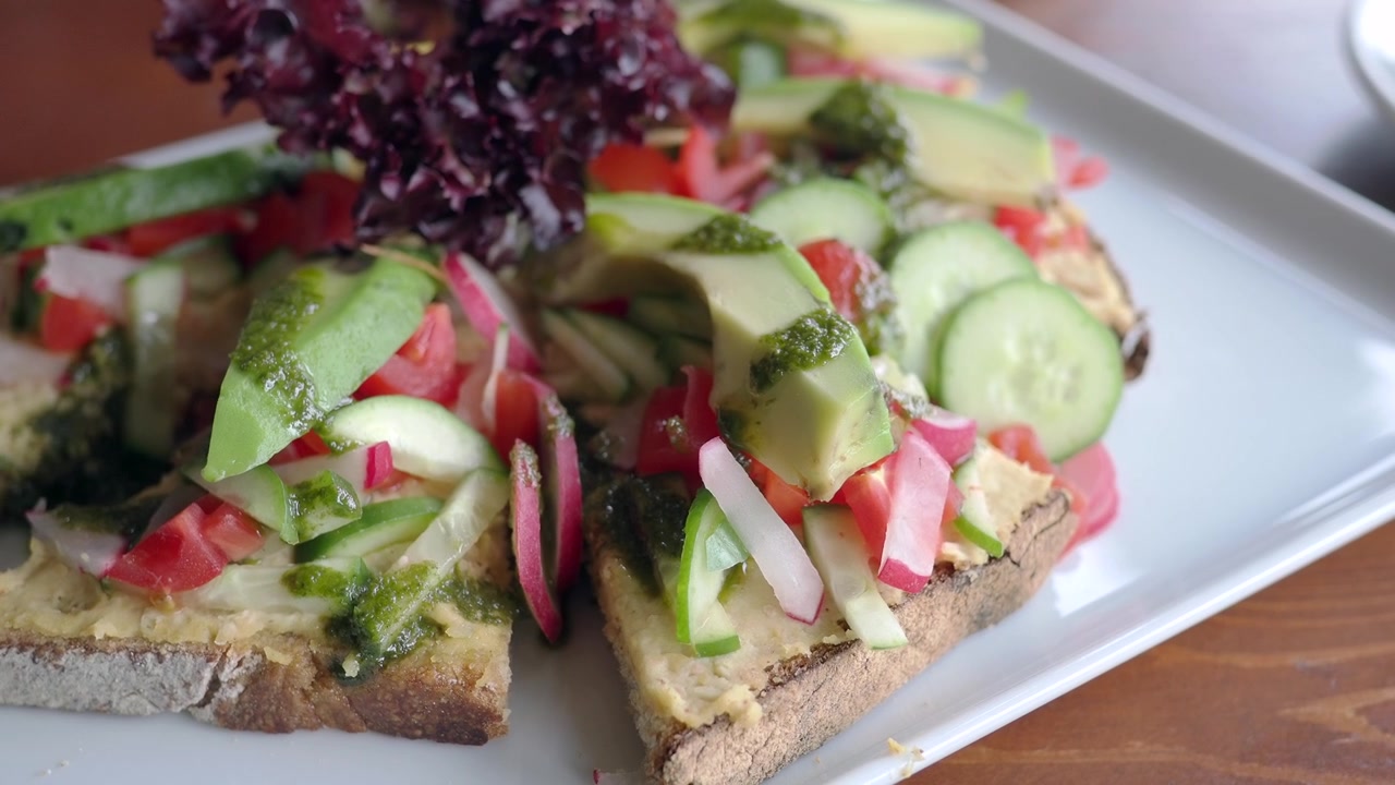 Gourmet avocadotoast med hummus, pesto og friske grøntsager.